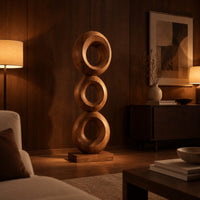 Stacked three ring sculpture with open centers on a flat plinth in an evening living room with walnut wall paneling