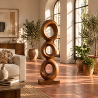 Stacked three ring sculpture with open centers on a flat plinth in a bright living room with arched windows and plants