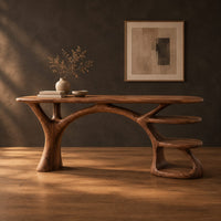 Wooden desk shaped like a tree with branching legs and two open shelves in a dark studio against a charcoal plaster wall