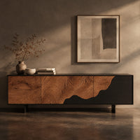 Corner detail of low tv stand with tree ring carving, a dark wave panel and birds beside wood, brass and linen samples