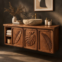 Corner detail of bathroom vanity cabinet with three tropical leaf carved doors and an open shelf beside wood, brass and linen samples
