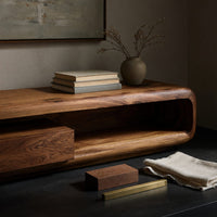 Corner detail of low capsule TV console with a drawer box and open end beside wood, brass and linen samples
