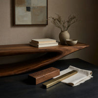 Corner detail of TV console with a curling hook top over drawers beside wood, brass and linen samples