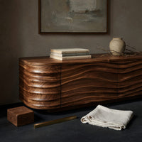 Corner detail of low TV stand with wave carved door fronts beside wood, brass and linen samples