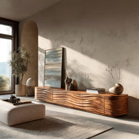 Low TV stand with wave carved door fronts in a sunlit room with large windows and plants