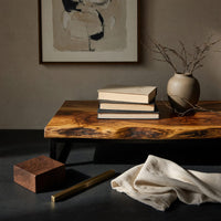 Corner detail of TV stand with figured wood doors on a black metal frame beside wood, brass and linen samples
