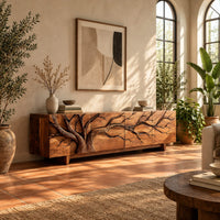 Tv stand with a carved branching tree across four front panels on tapered feet in a bright living room with arched windows and plants