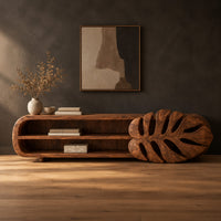 Low tv stand with two open shelves and a carved monstera leaf end in a dark studio against a charcoal plaster wall