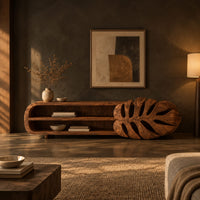 Low tv stand with two open shelves and a carved monstera leaf end in a dark living room at golden hour
