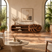 Low tv stand with two open shelves and a carved monstera leaf end in a bright living room with arched windows and plants
