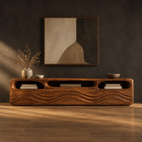 Low tv stand with carved wave relief on the front and open top cubbies in a dark studio against a charcoal plaster wall