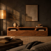 Low tv stand with carved wave relief on the front and open top cubbies in a dark living room at golden hour