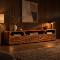 Low tv stand with carved wave relief on the front and open top cubbies in an evening living room with walnut wall paneling
