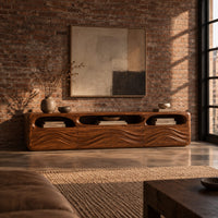 Low tv stand with carved wave relief on the front and open top cubbies in an industrial loft living room with exposed brick
