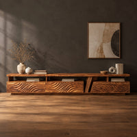 Long low tv stand with carved wave fronts and an open shelf above in a dark studio against a charcoal plaster wall