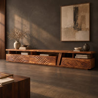 Corner detail of long low tv stand with carved wave fronts and an open shelf above beside wood, brass and linen samples