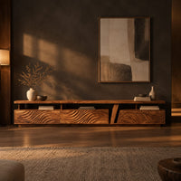 Long low tv stand with carved wave fronts and an open shelf above in a dark living room at golden hour