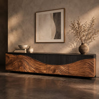 Corner detail of low tv stand with carved flowing grain panels under a dark top band beside wood, brass and linen samples