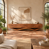 Low tv stand with a thick four panel body on a wavy ribbon base in a bright living room with arched windows and plants