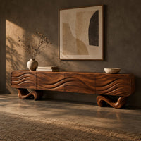 Corner detail of tv stand with four wave carved panels on two twisting ribbon feet beside wood, brass and linen samples
