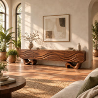 Tv stand with four wave carved panels on two twisting ribbon feet in a bright living room with arched windows and plants