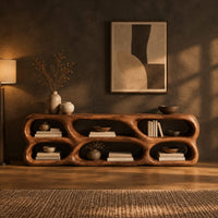 Low wooden tv stand with two rows of sculpted open cells in a dark living room at golden hour