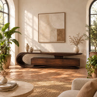 Tv stand with a sweeping loop end and low three panel cabinet in a bright living room with arched windows and plants