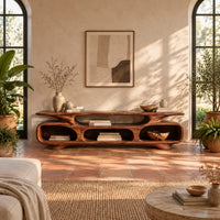 Low tv stand with three open oval cubbies under a sculpted slab top in a bright living room with arched windows and plants