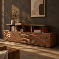 Corner detail of tv stand with wave carved front panels and a raised open display shelf beside wood, brass and linen samples
