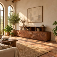 Tv stand with wave carved front panels and a raised open display shelf in a bright living room with arched windows and plants