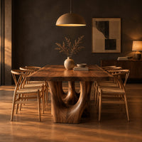 Dining table with a natural edge slab top and two sculpted arch legs in a dark dining room at golden hour