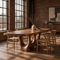 Dining table with a natural edge slab top and two sculpted arch legs in an industrial loft dining room with exposed brick