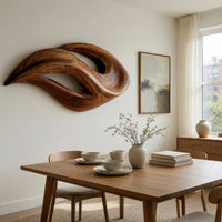 Twin crescent carved wood wall sculpture beside a dining table in natural light
