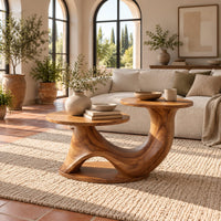 Coffee table with two disc tops at different heights on a swooping base in a bright living room with arched windows and plants