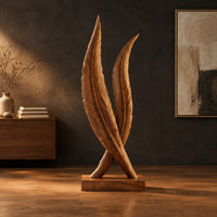 Twin feather sculpture with carved veins crossing over a solid wood plinth in a dark studio against a charcoal plaster wall