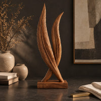 Corner detail of twin feather sculpture with carved veins crossing over a solid wood plinth beside wood, brass and linen samples