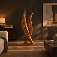 Twin feather sculpture with carved veins crossing over a solid wood plinth in a dark living room at golden hour