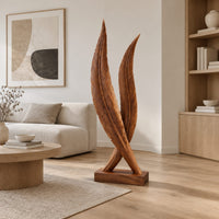 Twin feather sculpture with carved veins crossing over a solid wood plinth in a Scandinavian living room with white walls