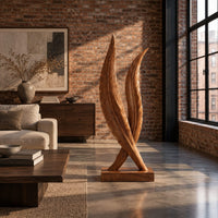 Twin feather sculpture with carved veins crossing over a solid wood plinth in an industrial loft living room with exposed brick