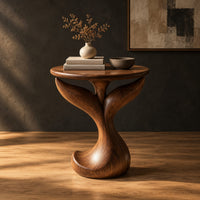 Pedestal side table with a round top, twin fins and a curled foot in a dark studio against a charcoal plaster wall