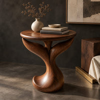 Corner detail of pedestal side table with a round top, twin fins and a curled foot beside wood, brass and linen samples