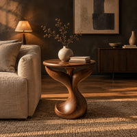 Pedestal side table with a round top, twin fins and a curled foot in a dark living room at golden hour