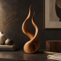 Corner detail of twin flame wood sculpture with two tall tips and a smooth teardrop base beside wood, brass and linen samples
