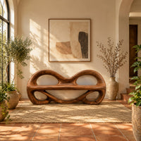 Wood bench with two looped openings above a flat plank seat in a bright entryway with arched windows and plants