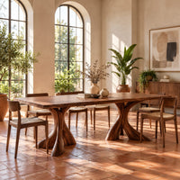 Rectangular dining table on two flared twisting pedestal bases in a bright dining room with arched windows and plants