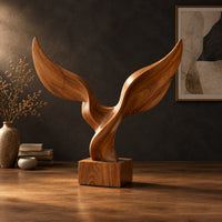 Twin wing sculpture with swept tips rising from a square wooden block in a dark studio against a charcoal plaster wall