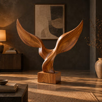 Twin wing sculpture with swept tips rising from a square wooden block in a dark living room at golden hour