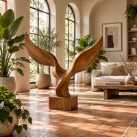 Twin wing sculpture with swept tips rising from a square wooden block in a bright living room with arched windows and plants