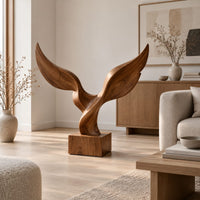 Twin wing sculpture with swept tips rising from a square wooden block in a Scandinavian living room with white walls