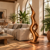 Tall floor lamp with a pointed tip, open twisting body and glowing edges in a bright living room with arched windows and plants